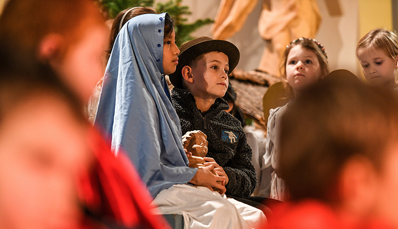 Kinder, als Maria und Josef verkleidet, halten die Holzfigur des Jesuskinds in den Armen bei einer Krippenfeier an Heiligabend, 24. Dezember 2018, in Bonn.
