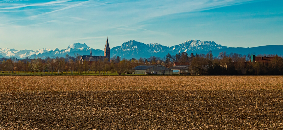 Fridolfing vor der Kulisse der Berchtesgadener Alpen mit der Pfarrkirche Mariä Himmelfahrt, die auch als Salzachdom oder Dom des Rupertiwinkels bezeichnet wird.