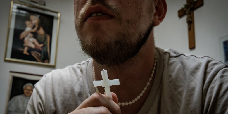 Ein Gefangener hält ein Kreuz, das er an einer Kette am Hals trägt.
