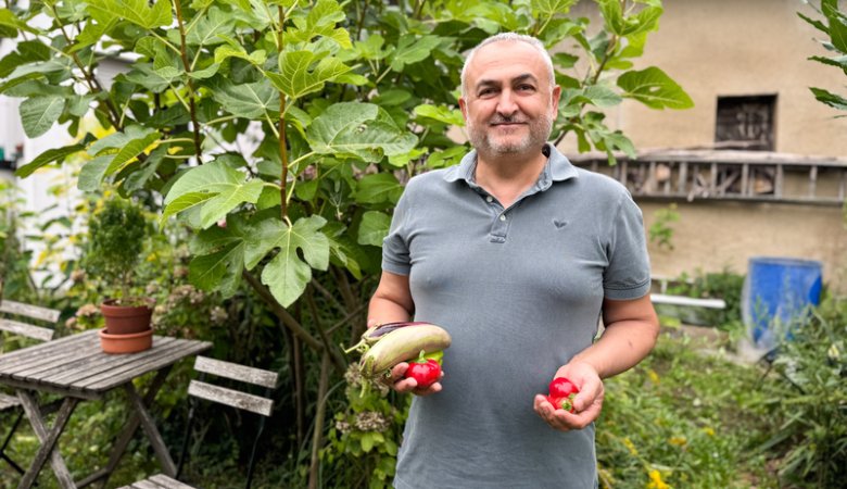 Hobbygärtner Tahsin Es in seinem Garten mit geerntetem Gemüse, Tomaten und Gurke.