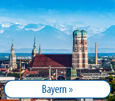 Stadtansicht von München mit der Frauenkirche im Vordergrund und den Alpen im Hintergrund, blauer Himmel. Text: 
