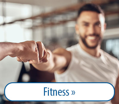 Zwei Personen geben sich einen Faustgruß in einem Fitnessstudio. Im Vordergrund ist eine Faust zu sehen, im Hintergrund eine lächelnde Person in Sportkleidung. Text: 