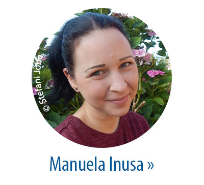 Porträtfoto von Manuela Inusa vor blühenden Hortensien, lächelnd in die Kamera schauend.