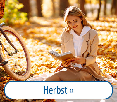 Frau sitzt im Herbstlaub und liest ein Buch, neben ihr ein Fahrrad.