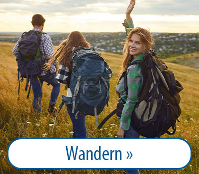 Drei Personen wandern über eine Wiese mit Rucksäcken. Eine Frau im Vordergrund lächelt und winkt. Im Hintergrund ist eine Landschaft mit Hügeln und einem Dorf zu sehen. Unten steht der Text 